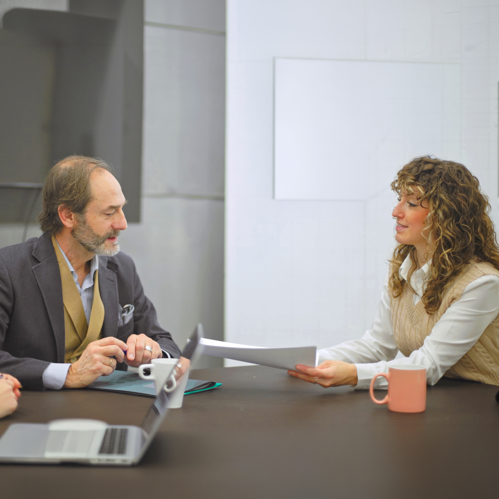 Woman in a white shirt and beige jumper presenting a document to a colleague during a meeting